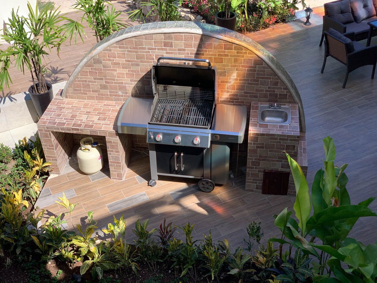 An outdoor kitchen with a grill, a sink, and a gas tank.