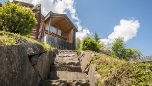 A wooden cabin with a stone staircase leading to a wooden deck. - Vacation Home "Haus der Sinne Bregenzerwald" with Mountain View & Balcony (Egg-Kaltenbrunnen)