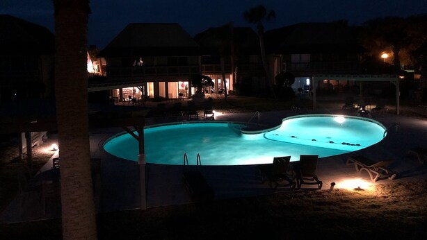 A nighttime view of a swimming pool area with lounge chairs and a building in the background. - Pool + Ocean View + Walk to Beach - Villa (Fripp Island)