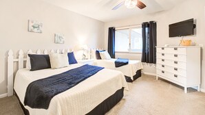 A bedroom with two beds, a ceiling fan, a dresser, a TV, and a window with curtains. - Pool + Ocean View + Walk to Beach - Villa (Fripp Island)
