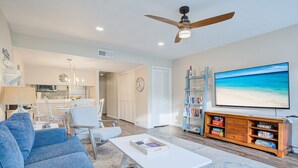 A living room with a sofa, coffee table, TV, bookshelf, and a dining area with chairs and a table. - Pool + Ocean View + Walk to Beach - Villa (Fripp Island)