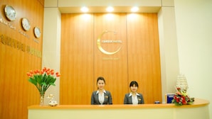 Una recepción de hotel con dos empleados, un reloj y un cartel que dice 'CENTRE HOTEL'.