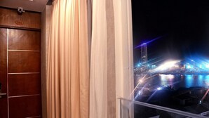 Vista desde una ventana con cortina, que muestra un paisaje urbano nocturno con edificios iluminados y un puente.