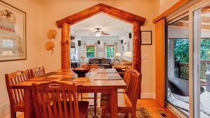 A dining area with a wooden table and chairs, a ceiling fan, and a view of the kitchen and living room through an open archway.