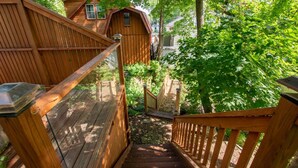 A wooden staircase leading to a small wooden structure with a window, surrounded by lush greenery.