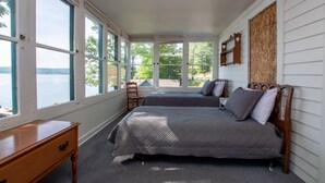 Une chambre avec deux lits, un bureau en bois et de grandes fenêtres donnant sur un plan d’eau.