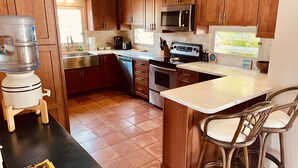 A kitchen with wooden cabinets, stainless steel appliances, a water dispenser, and a bar stool. - Stunning Paradise Overlook - Incredible Views from Every Room (Christiansted)