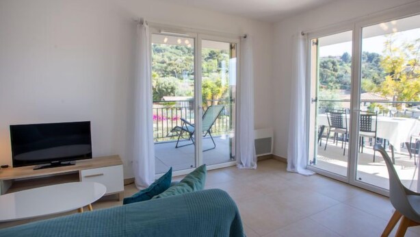 Un dormitorio moderno con televisión, cama y balcón con mobiliario exterior.