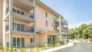 Un edificio residencial de varios pisos con balcones, ventanas amplias y un camino de entrada pavimentado.