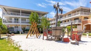 A beachfront hotel with multiple balconies, a sandy beach area with wooden structures, and a clear blue sky.