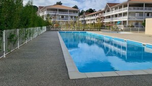 A swimming pool with a tiled deck, surrounded by a white fence and buildings with balconies.