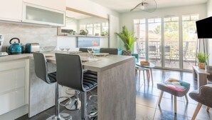 A modern kitchen with bar stools, a dining area with a table and chairs, and a balcony with a view.