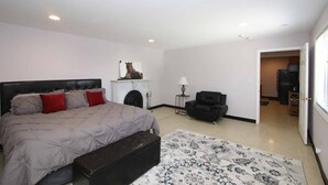 Un dormitorio con cama, chimenea, una silla y una puerta que da a otra habitación.