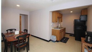 Una cocina compacta con armarios de madera, un refrigerador negro y un pequeño comedor con mesa y sillas.