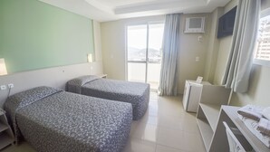Habitación de hotel con dos camas, un escritorio, una silla, un televisor y un balcón con cortinas.