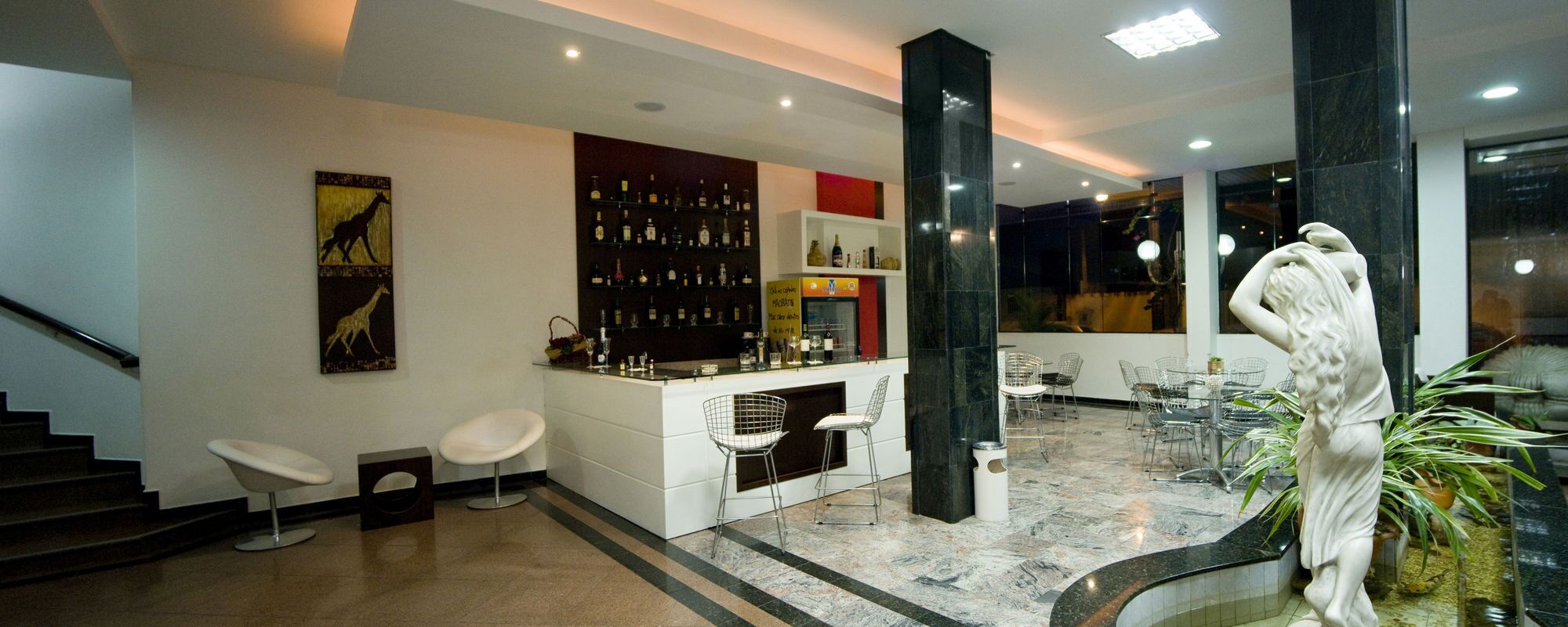 Uma área de bar moderna com piso de mármore, banquetas brancas e variedade de garrafas de bebidas alcoólicas.