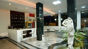 Zona de bar moderna con suelo de mármol, taburetes blancos y una variedad de botellas de licor.