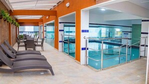 Un área de piscina interior con sillones de descanso, mesa de billar y un espacio de estar con sillas y mesas.