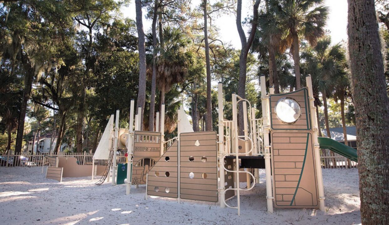 A playground with climbing structures and slides, surrounded by trees.