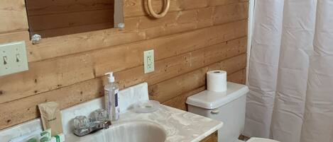 Ein Badezimmer mit Holzwandverkleidung, ausgestattet mit einem Waschbecken, einem Waschtisch, einer Toilette und einer Duschvorhang.