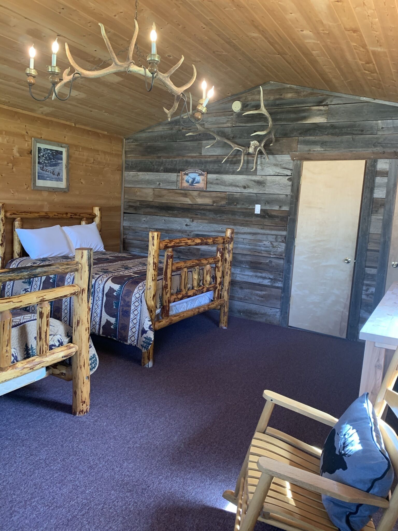 Ein rustikales Zimmer mit einem hölzernen Bett, einem Holzstuhl und einer aus Geweihen gefertigten Kandelaber.