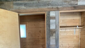 Un interior de madera con una puerta que da a un baño, una ventana y una estantería.