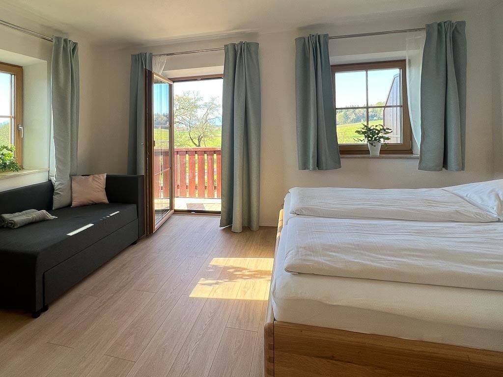 Un dormitorio con cama, sofá y balcón con cortinas.