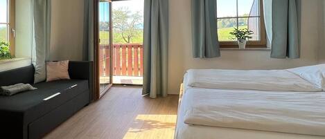 Un dormitorio con cama, sofá y balcón con cortinas.