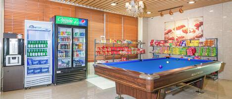 A pool table in a brightly lit room with wooden ceiling panels and a vending machine selling beverages.
