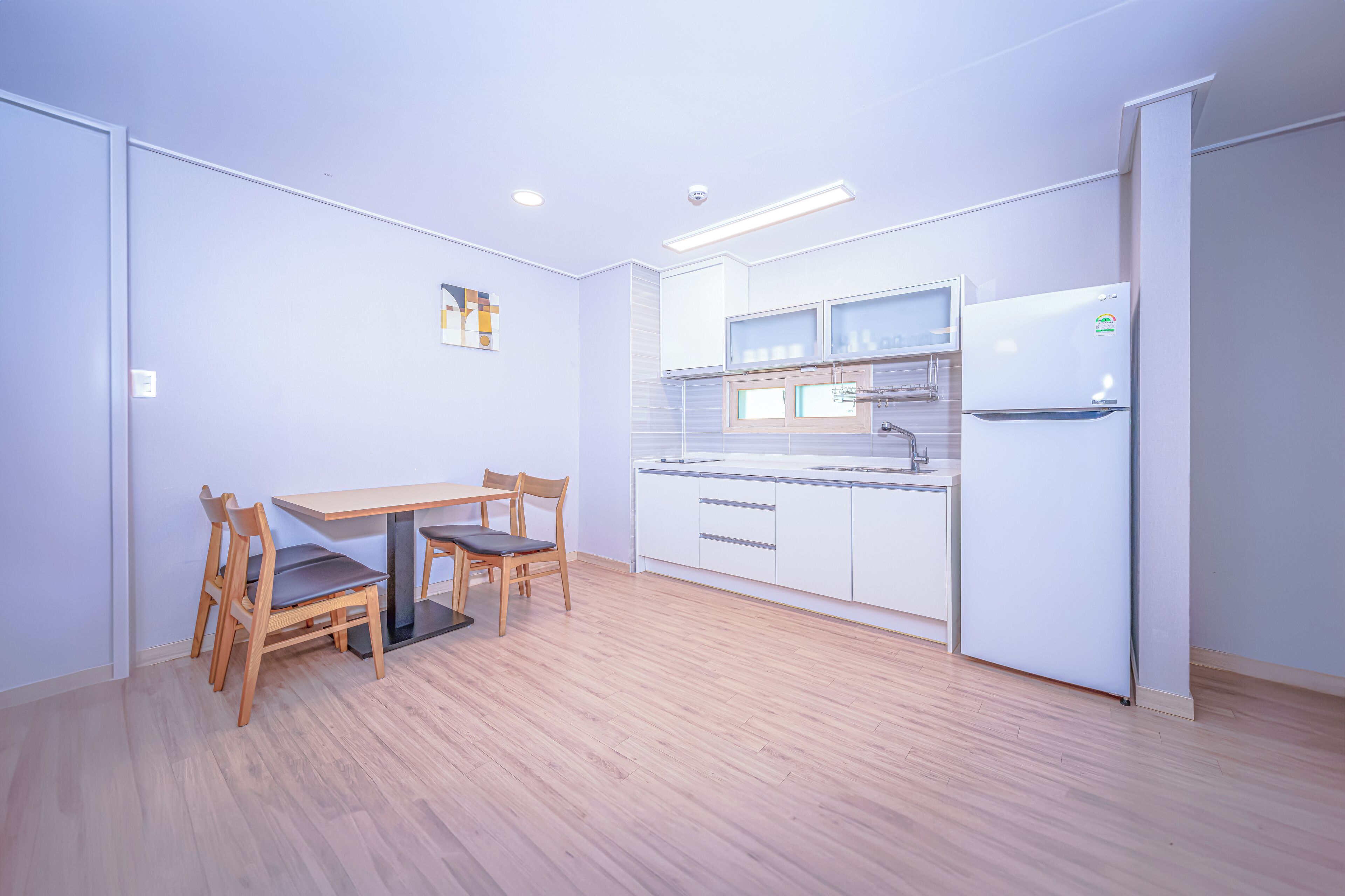Una cocina moderna con una mesa de comedor y sillas, armarios blancos y un refrigerador.