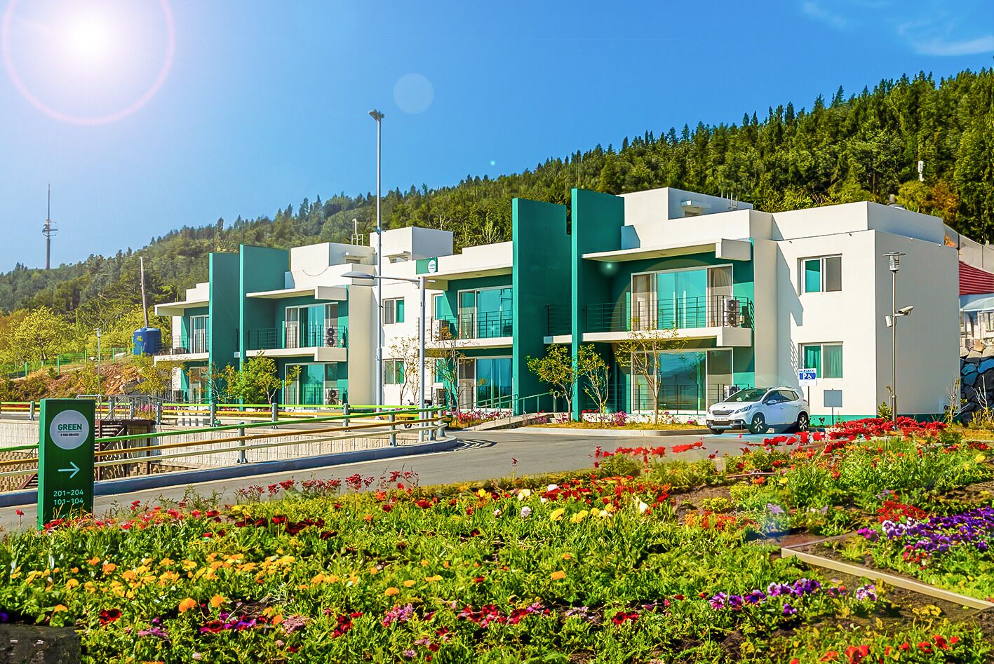 Een modern gebouw met een parkeerplaats en een groen bord met routeaanduidingen.