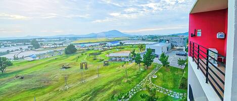 A view from a balcony overlooking a green landscape with a river, buildings, and a mountain in the distance.
