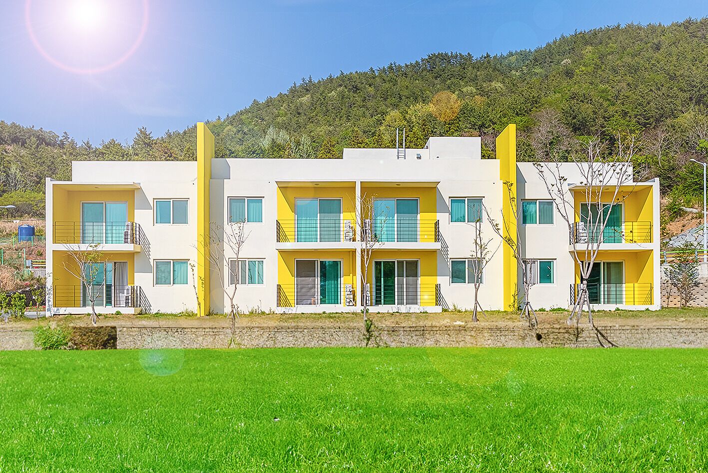 Un edificio moderno de varios pisos con balcones, con un paisaje montañoso de fondo.