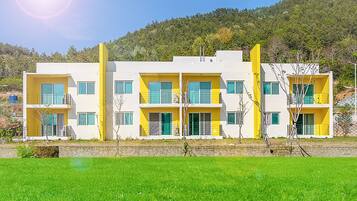 Un edificio moderno de varios pisos con balcones, con un paisaje montañoso de fondo.