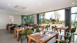A modern dining area with wooden tables and chairs, large windows offering a view of the outdoors.