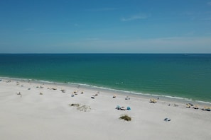 Une plage de sable blanc bordée d’une eau d’un bleu cristallin. Plusieurs parasols et chaises de plage sont disposés le long du rivage.