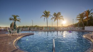 Ein Swimmingpool mit Liegestühlen und Palmen, umgeben von einer Ziegelterrasse.