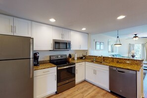 Une cuisine moderne avec des armoires blanches, des appareils en acier inoxydable, des comptoirs en granit et un ventilateur de plafond.