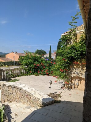 A courtyard with stone walls, a fountain, and red flowers. - Maison de Vacances en Provence Verte (Carcès)