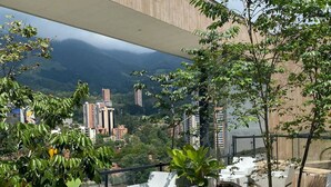 Eine Terrasse im Freien mit moderner Sitzgelegenheit und Blumentöpfen, mit Blick auf Stadt und Berge.