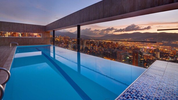 Ein schimmernder Infinity-Pool auf dem Dach mit Blick auf die Stadt bei Einbruch der Dunkelheit.