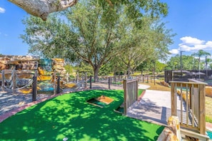 Ein Spielplatz mit grüner Kunstrasenfläche, Holzspielgeräten und einer Felsenformation.