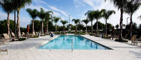 A rectangular swimming pool with a clear blue water surface, surrounded by a tiled deck with lounge chairs and palm trees.