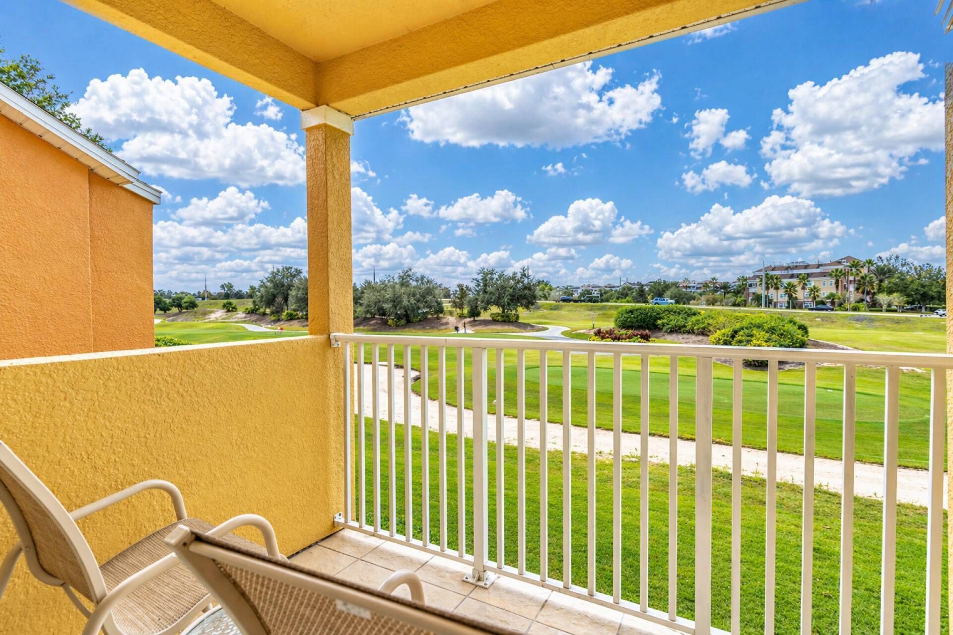 Un balcón con vista a un campo de golf, una silla y un edificio al fondo.