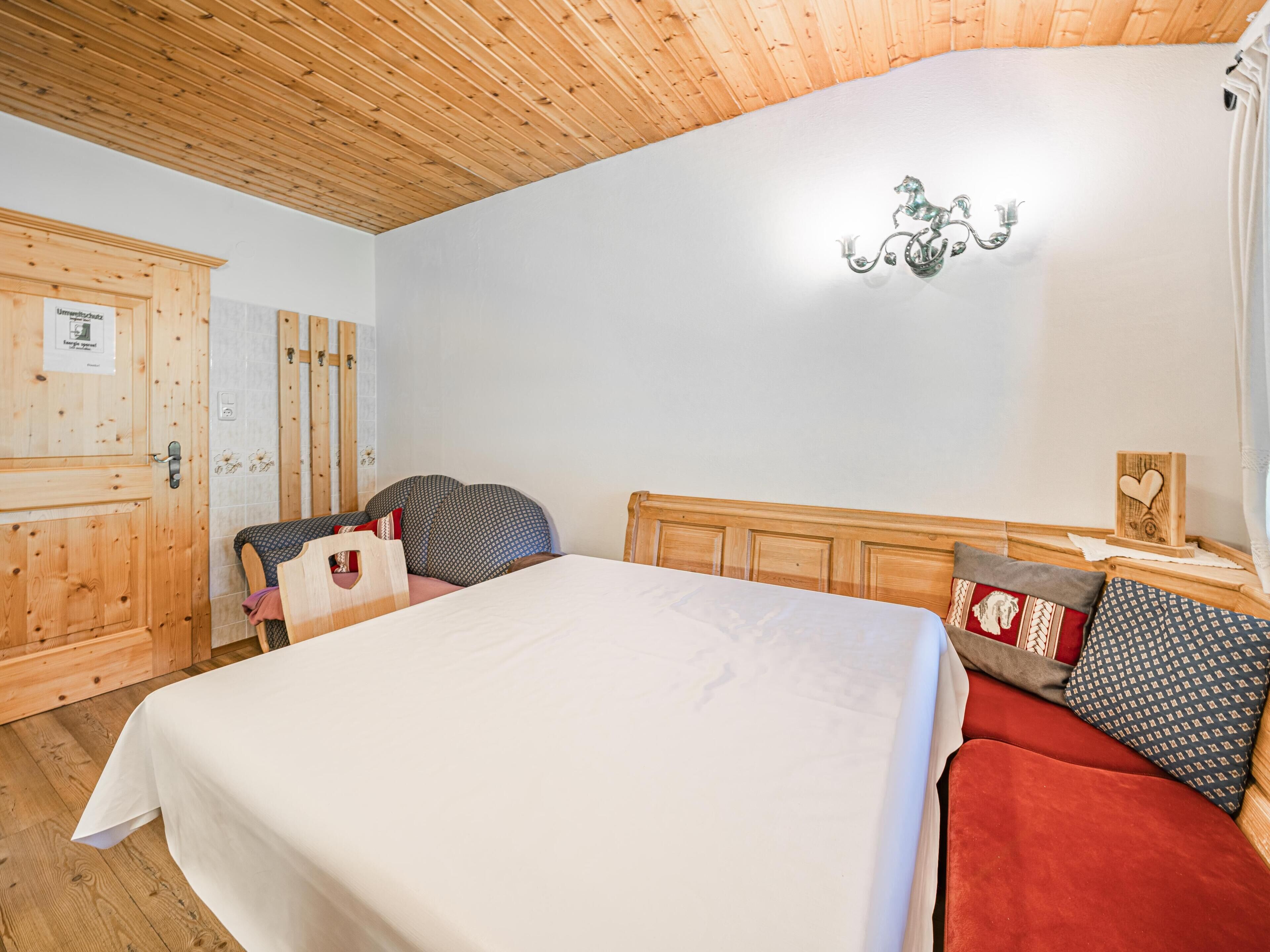 Un dormitorio con techo de madera, una cama con colcha blanca, cabecera de madera y mesita de noche con un objeto decorativo.