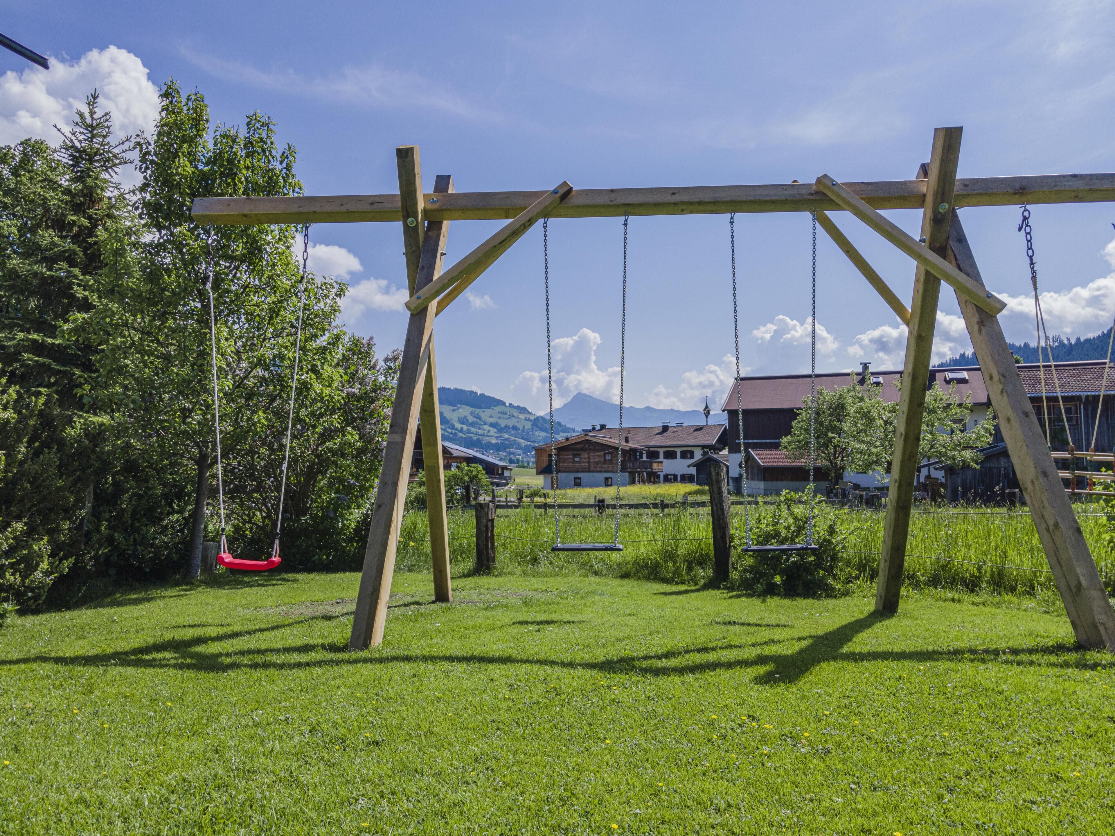 A wooden swing set in a grassy area with houses and mountains in the background.