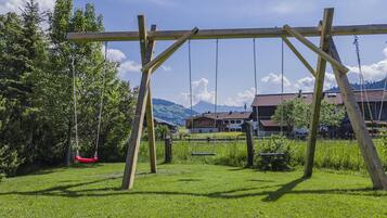 A wooden swing set in a grassy area with houses and mountains in the background.