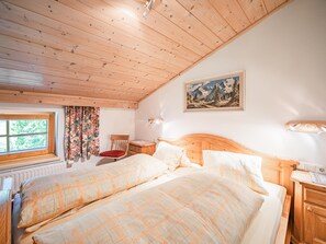 A bedroom with two beds, wooden ceiling, a window, a chair, a painting, and a nightstand. - Holiday home on former farm (Brixen im Thale)