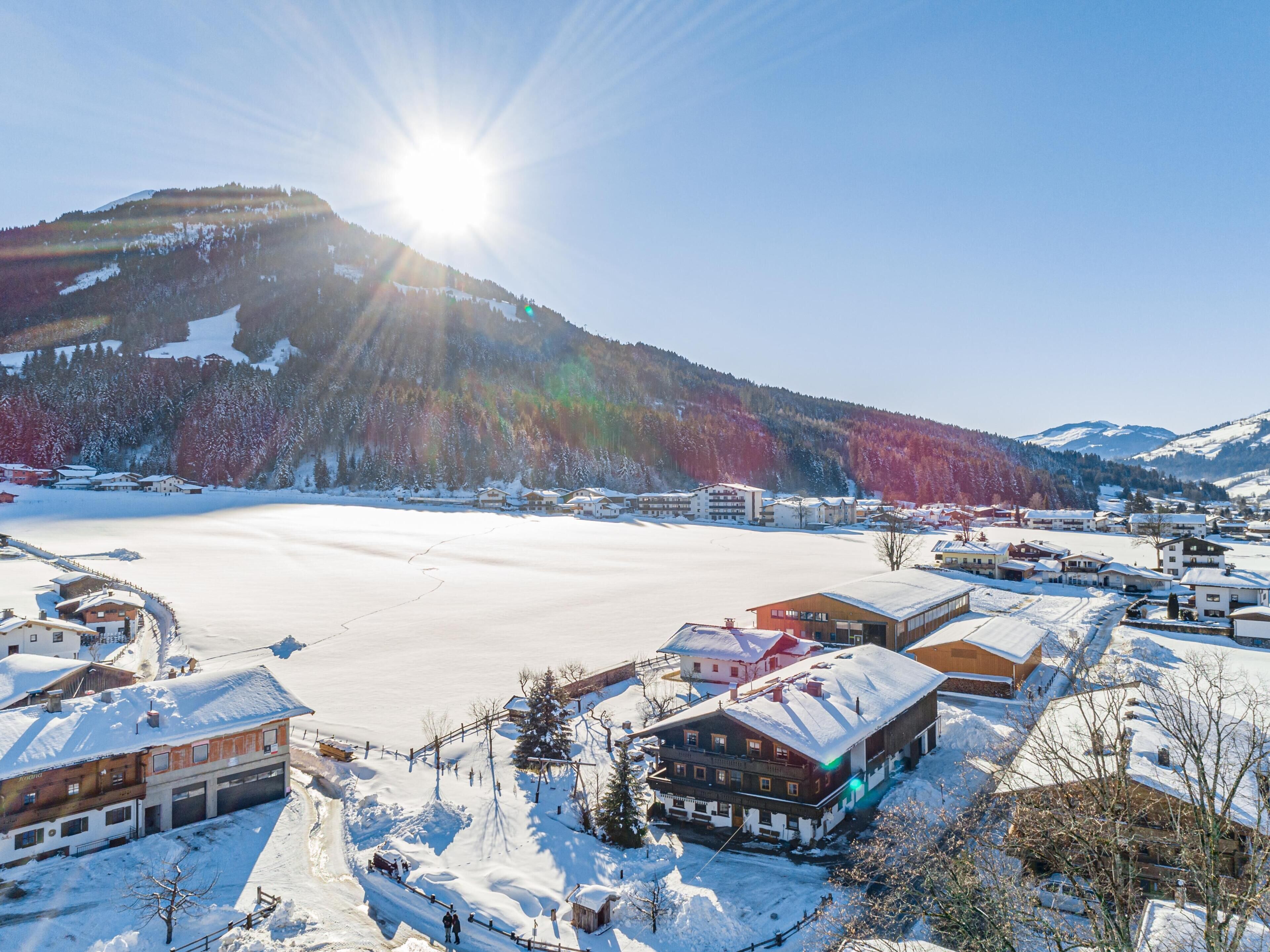 Ein verschneites Dorf mit Gebäuden, einem zugefrorenen See und Bergen im Hintergrund.