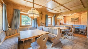 En inredning med träpaneler, ett stort matbord i mitten, bänkar och ett stort fönster.